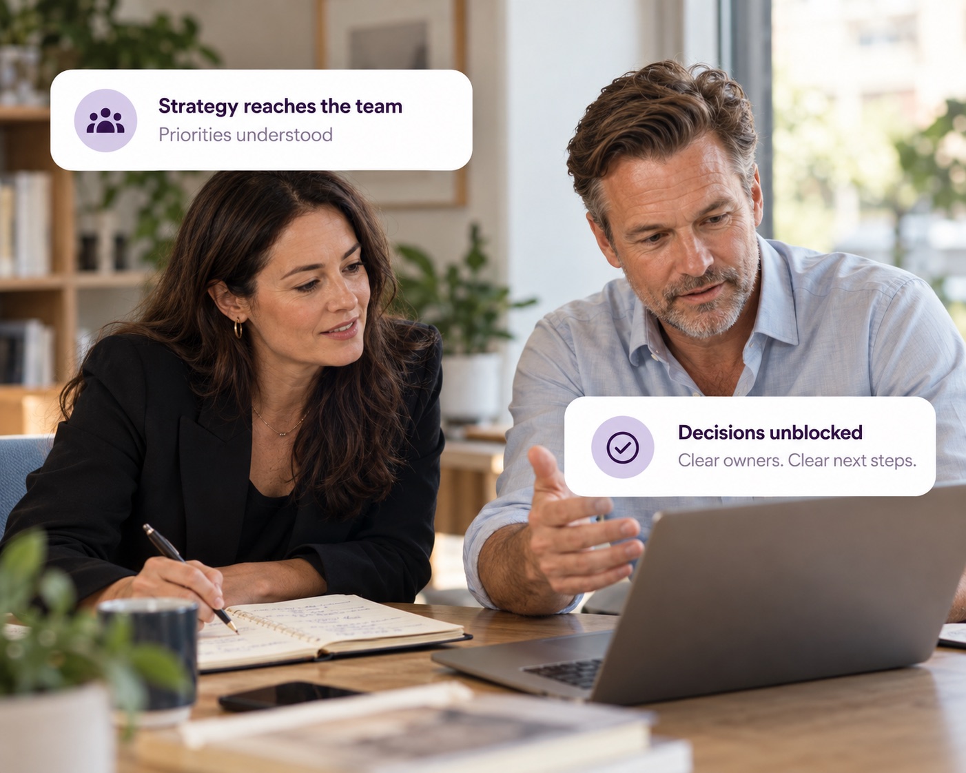 Two executives reviewing work at a laptop, with Decided cards showing strategy reaching the team and decisions unblocked